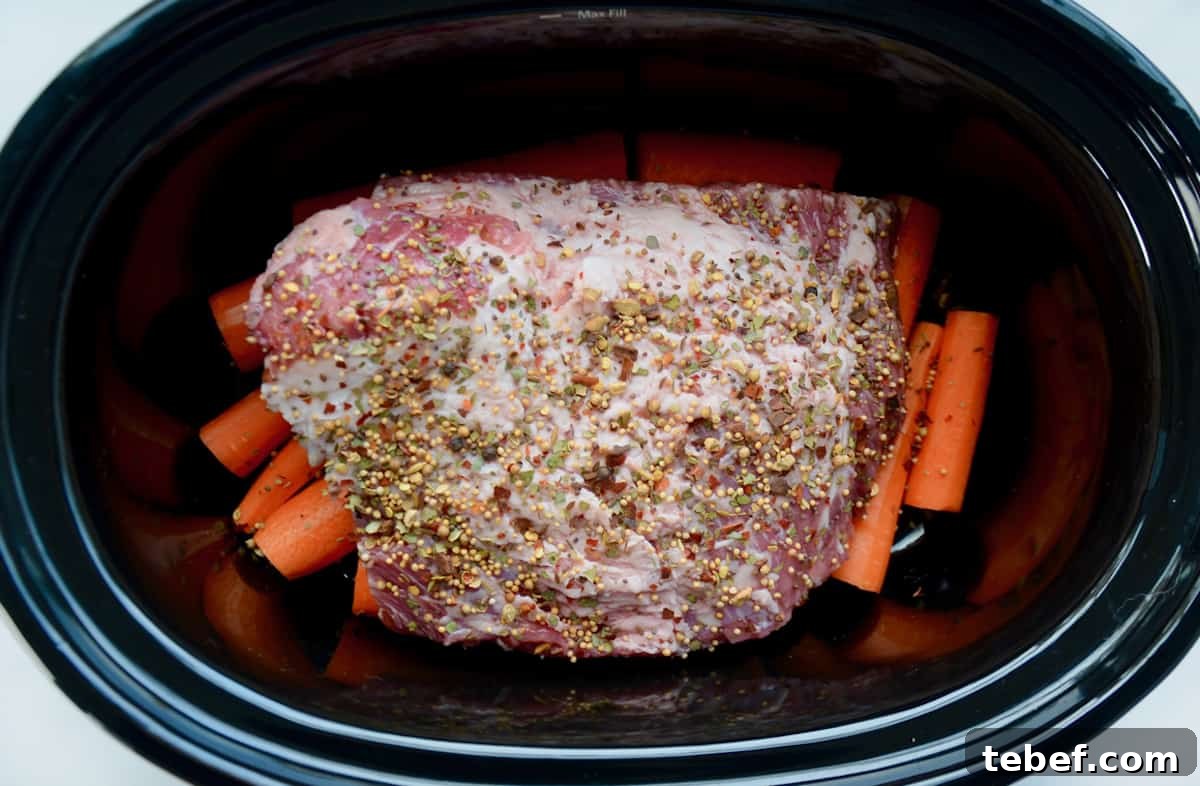Corned beef sits on a bed of carrots in a slow cooker crock.