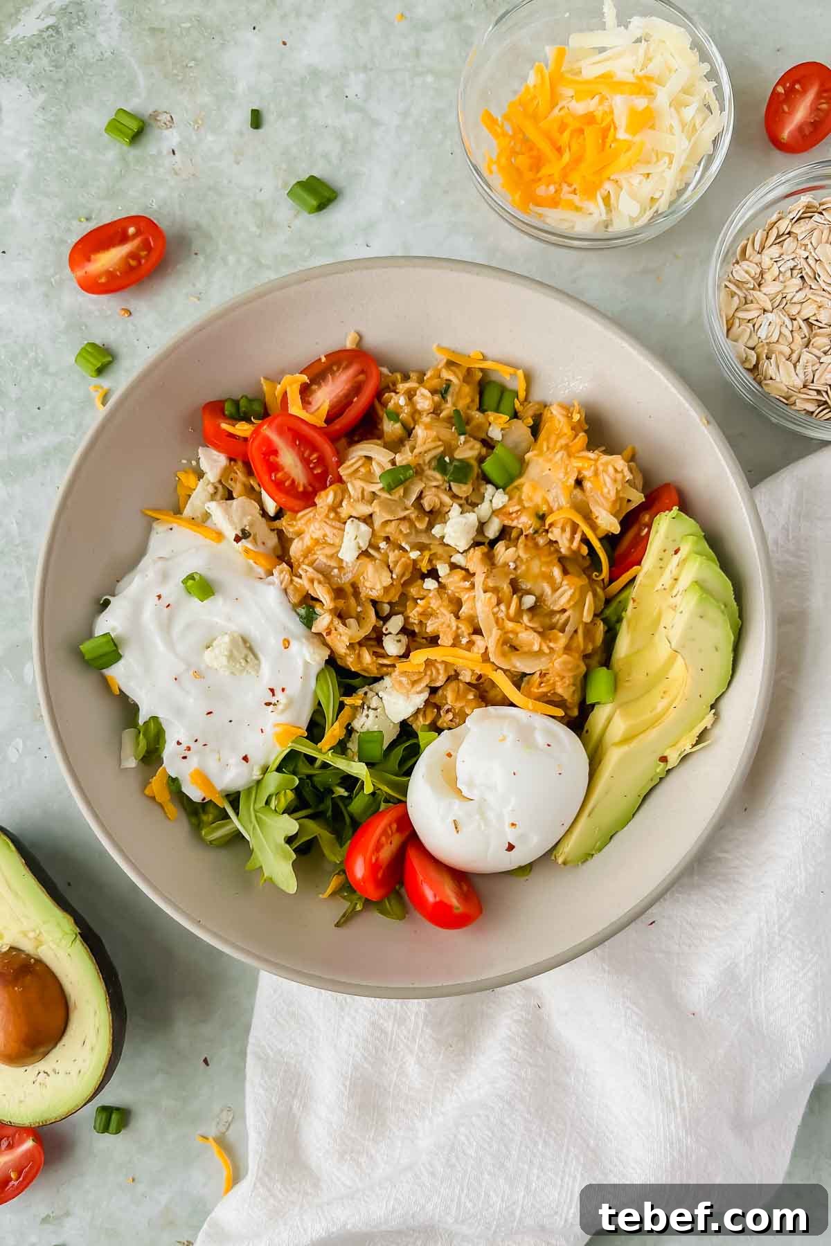Savory Cheesy Oatmeal Recipe: Comforting Savory Oats in 15 Minutes 9 cheesy oatmeal topped with avocado, egg, yogurt, and herbs in a ceramic bowl on a gray slate background.