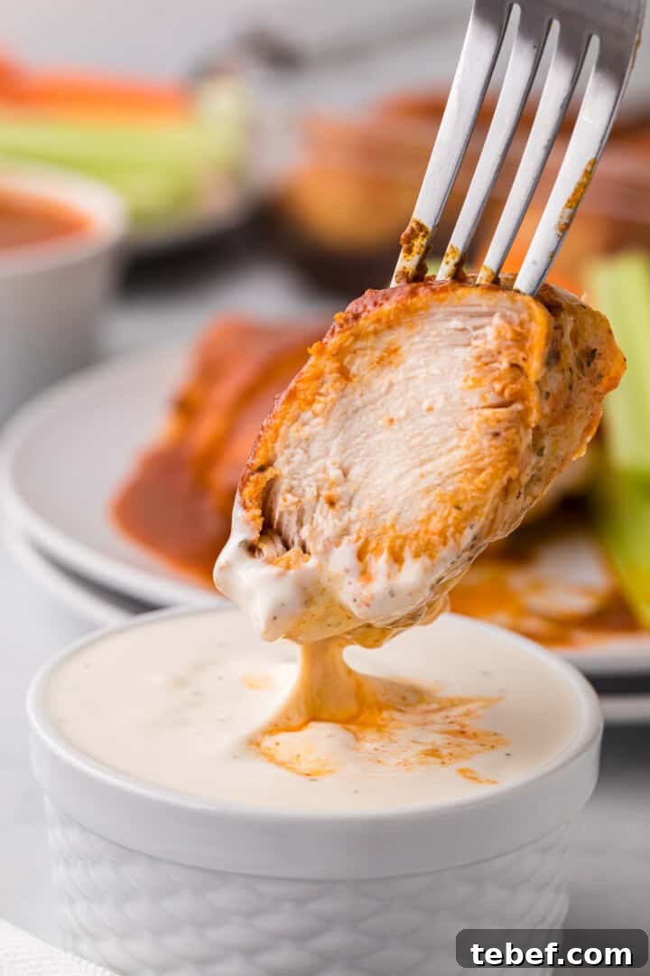 Oven-Baked Buffalo Chicken Thighs with Crispy Skin 11 dipping piece of baked Buffalo chicken into ranch dressing.