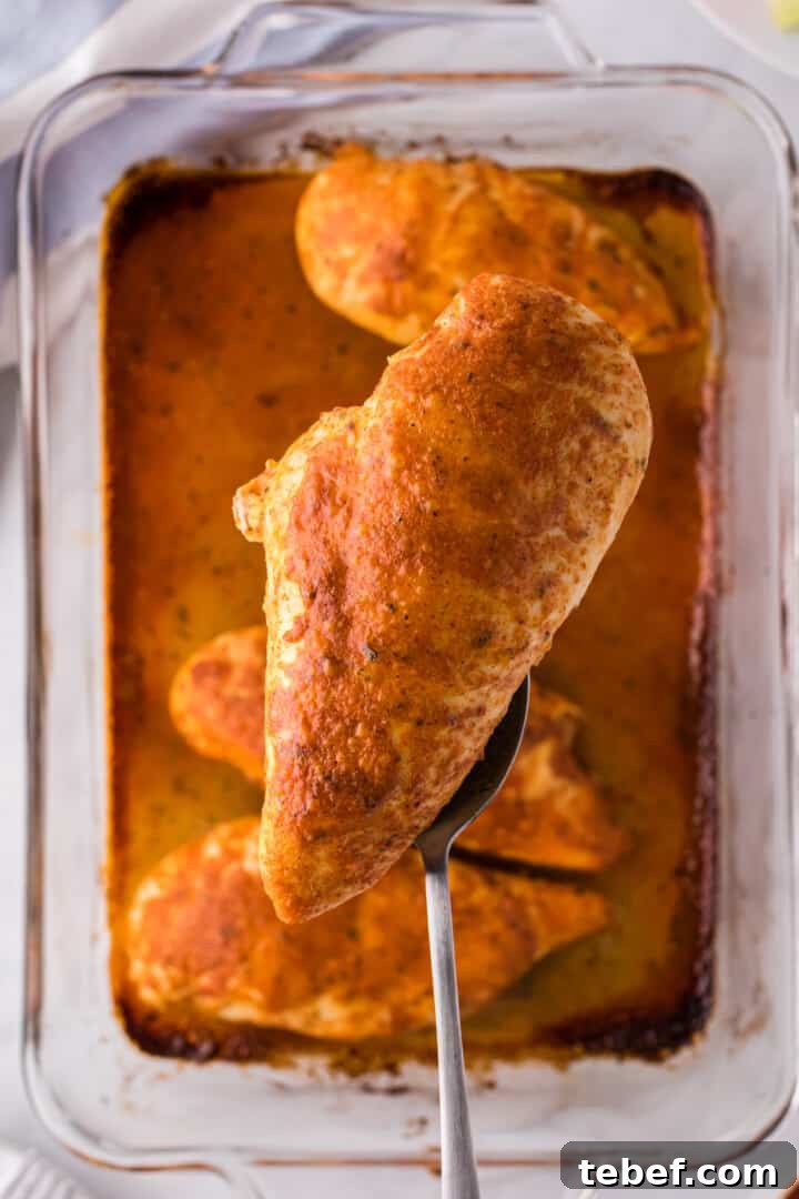 Oven-Baked Buffalo Chicken Thighs with Crispy Skin 8 chicken lifted out of the baking dish with fork.