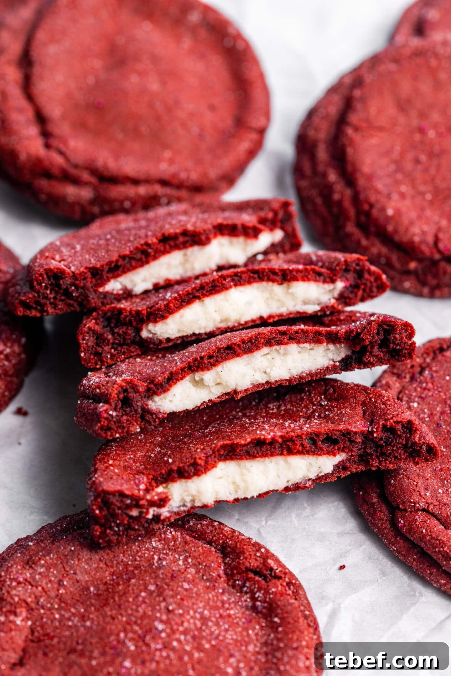 Red Velvet Cookies Stuffed with Cream Cheese — 8 Giant Cookies 5 Cream cheese stuffed red velvet cookies on top of parchment paper; some are split in half showing off the cream cheese filling in the center.