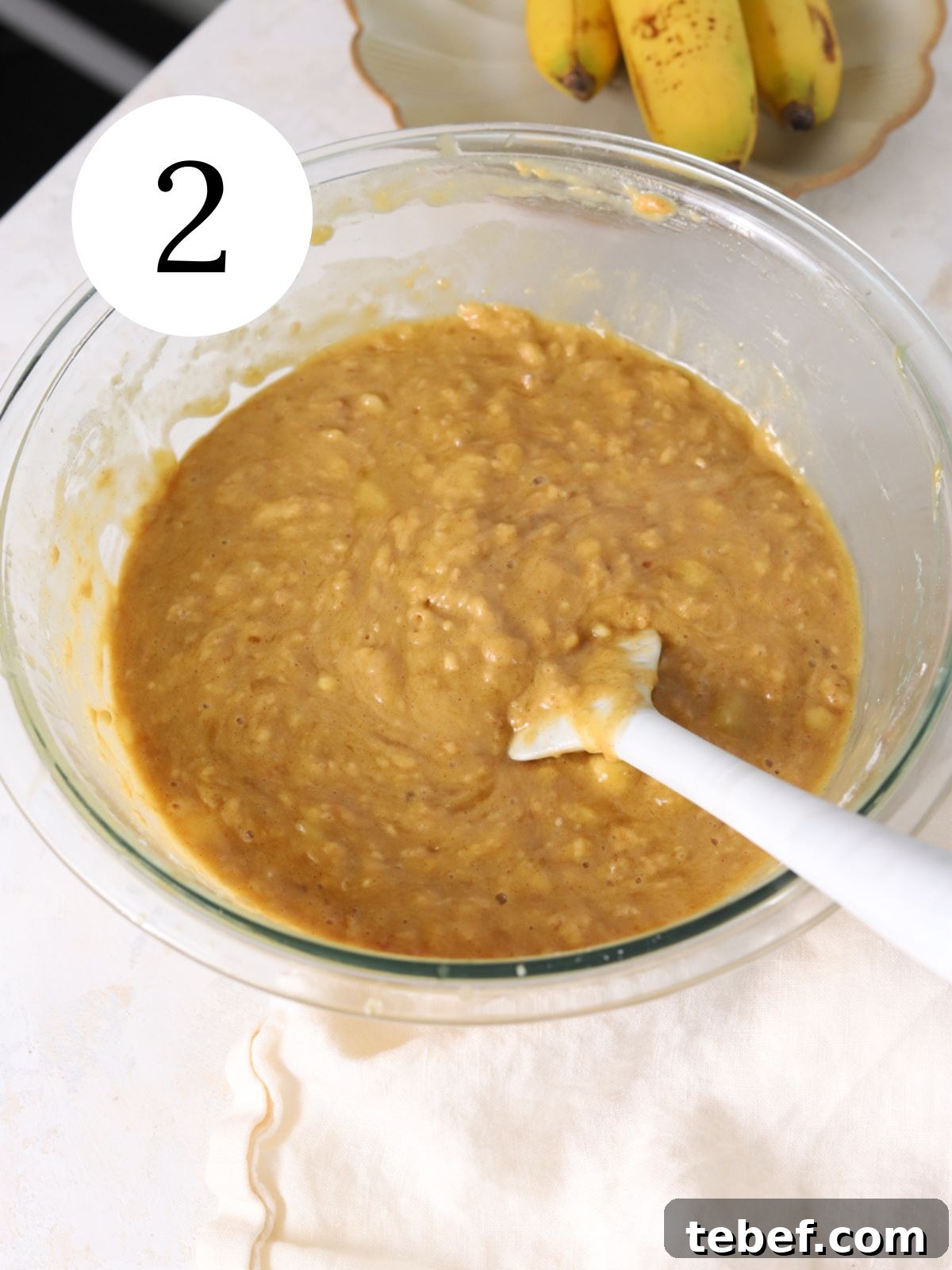 Moist Banana Olive Oil Cake Recipe for Perfect Homemade Dessert 5 Banana cake batter in a glass bowl with a spatula.