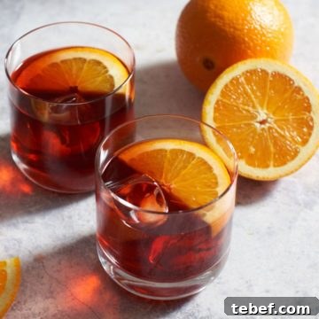 Two mezcal negronis next to sliced oranges.