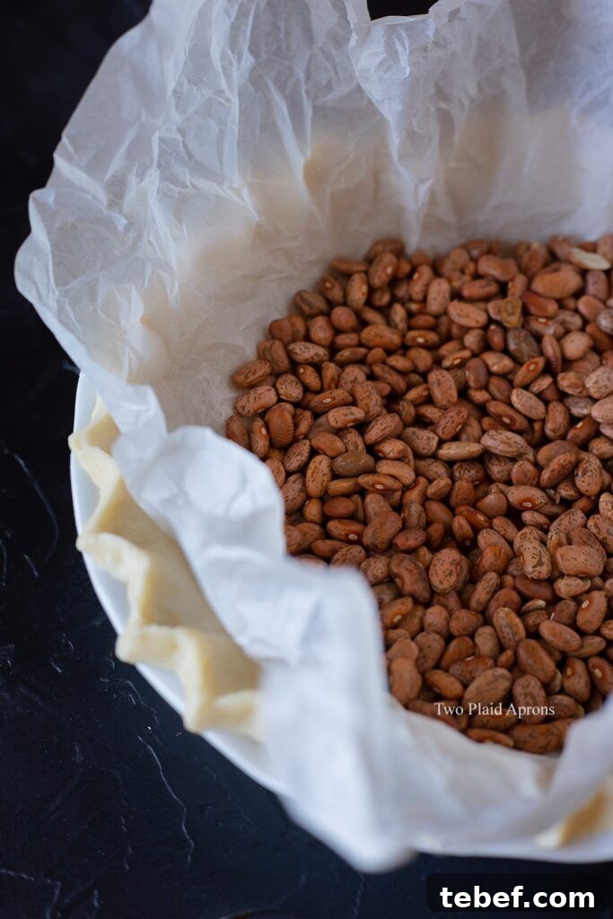 Raw pie crust with baking beans lined with crumbled parchment.