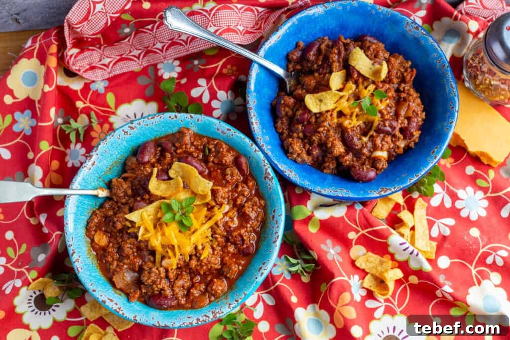 30-Minute Hearty Chili Recipe for Weeknight Dinners 2 Two bowls of chili topped with corn chips and grated cheese sit on a orange flowered cloth.
