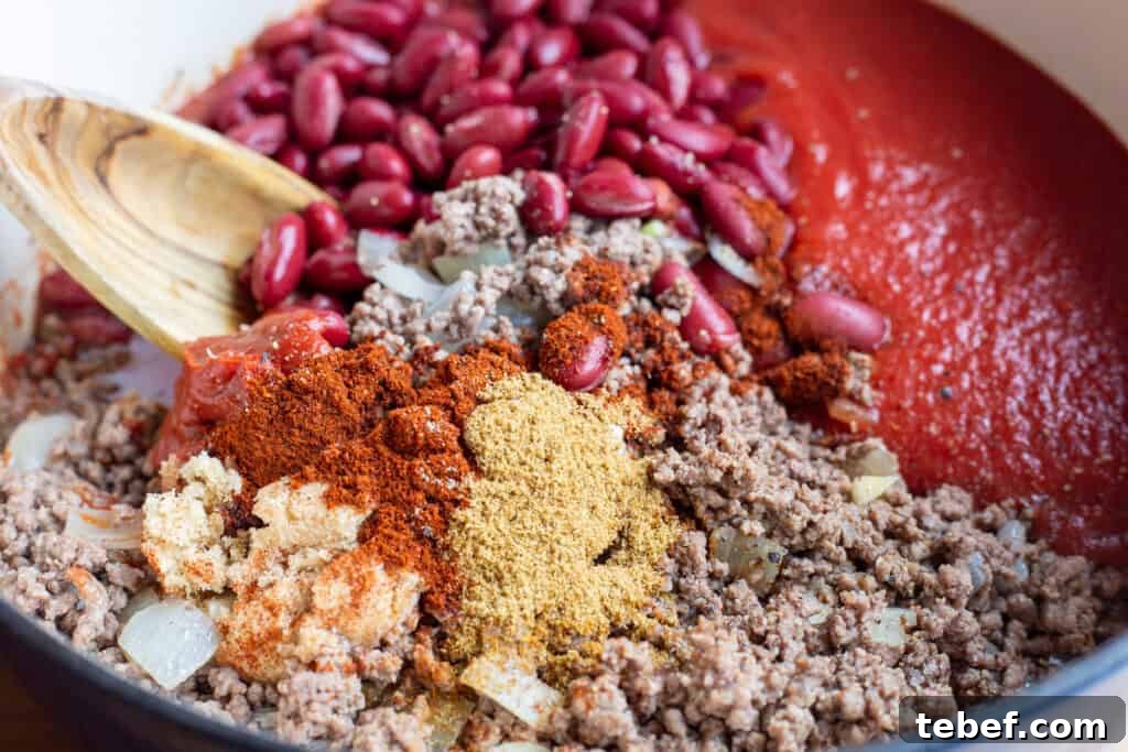 30-Minute Hearty Chili Recipe for Weeknight Dinners 3 Ingredients for homemade chili in a large blue pot with a wooden spoon off to the side.