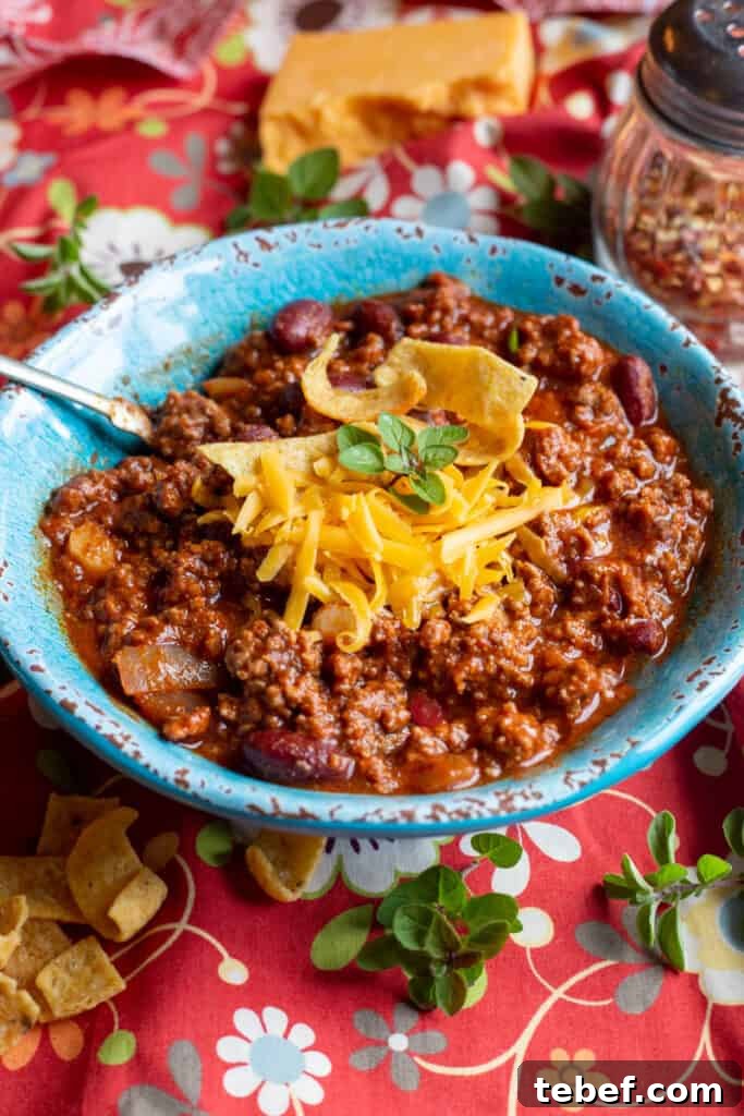 30-Minute Hearty Chili Recipe for Weeknight Dinners 4 A blue bowl filled with chili sits on an orange-floured cloth. Around the bowl is scattered corn chips and herbs.