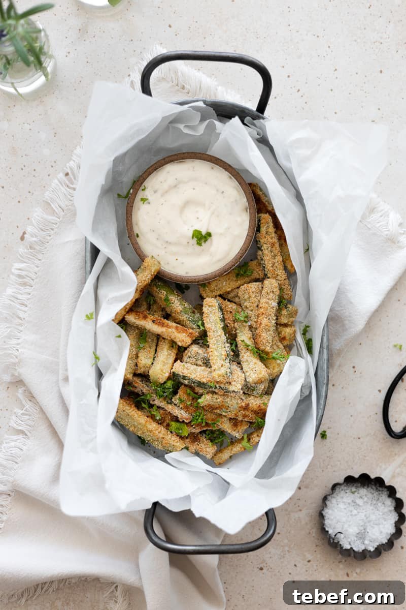 A basket of baked zucchini slices with a small bowl of garlic aioli dipping sauce. 