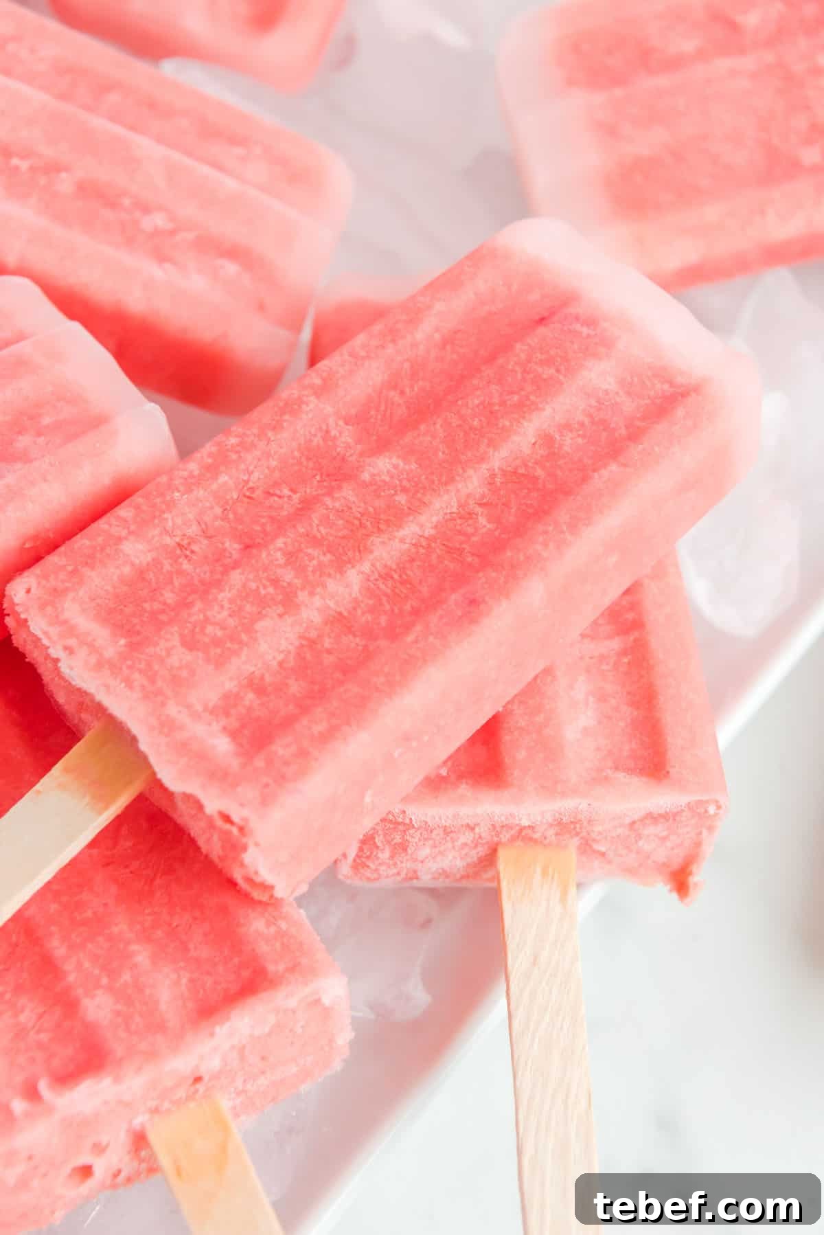 Refreshing Watermelon Popsicle Recipe: 3-Ingredient Frozen Treats 11 A close-up, angled photo of a plate of ice cubes topped with watermelon popsicles stacked on top of each other.
