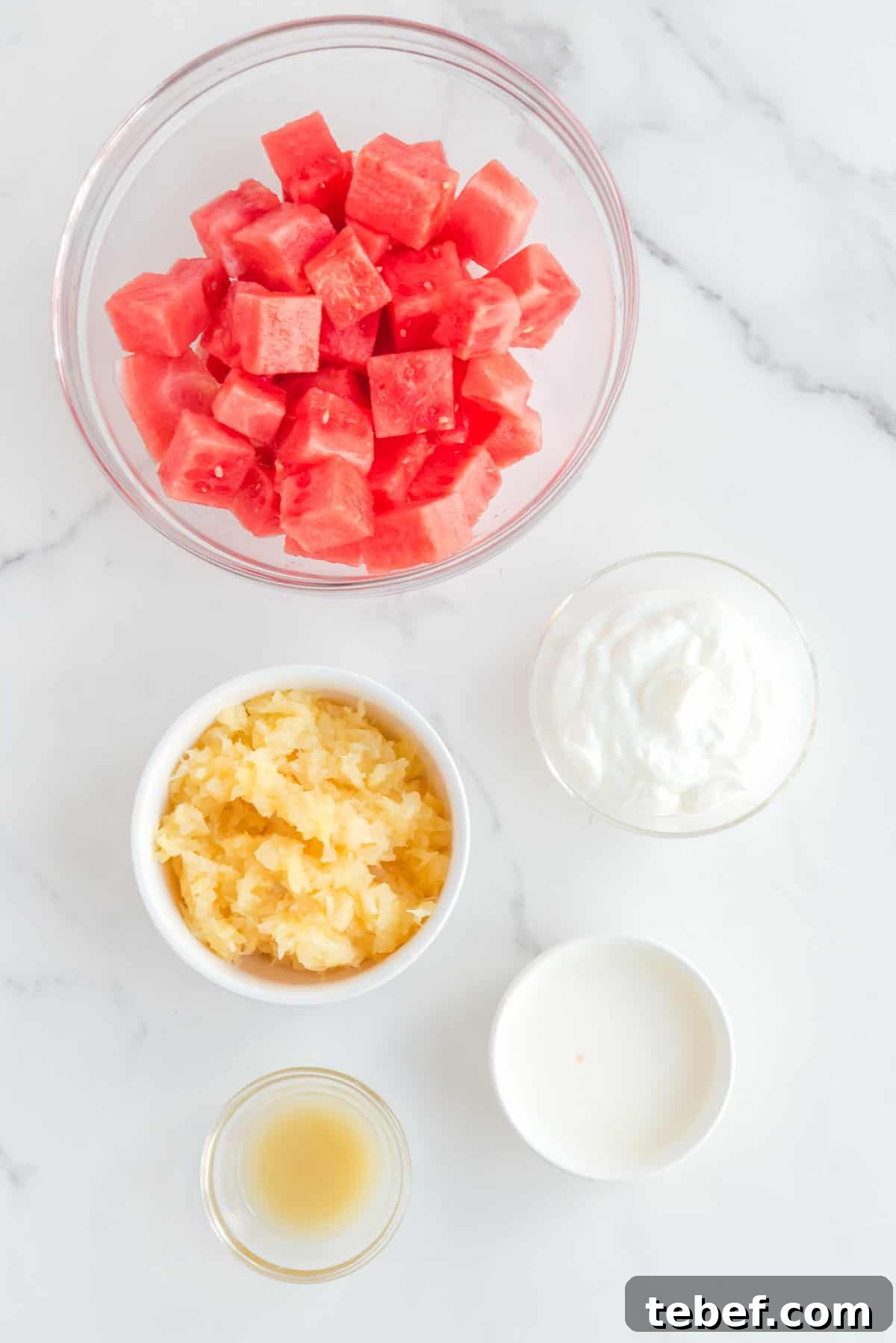 Refreshing Watermelon Popsicle Recipe: 3-Ingredient Frozen Treats 4 Watermelon popsicle ingredients separated in small bowls: cubed watermelon, crushed pineapple, greek yogurt, heavy cream and lemon juice.