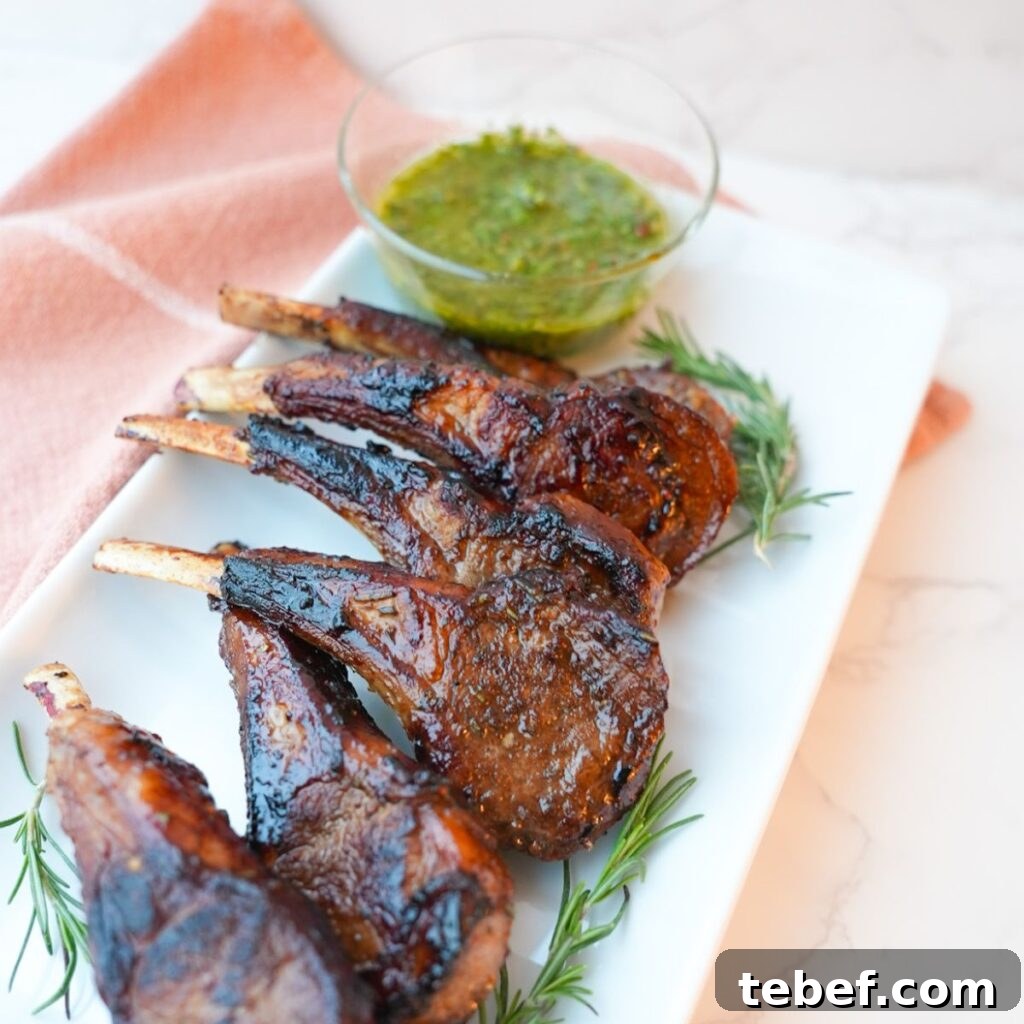 Garlic Herb Lamb Chops with Crispy Seared Edges 12 Lamb chops with a side of mint chimichurri on a plate with visible herbs and a glossy seared crust.
