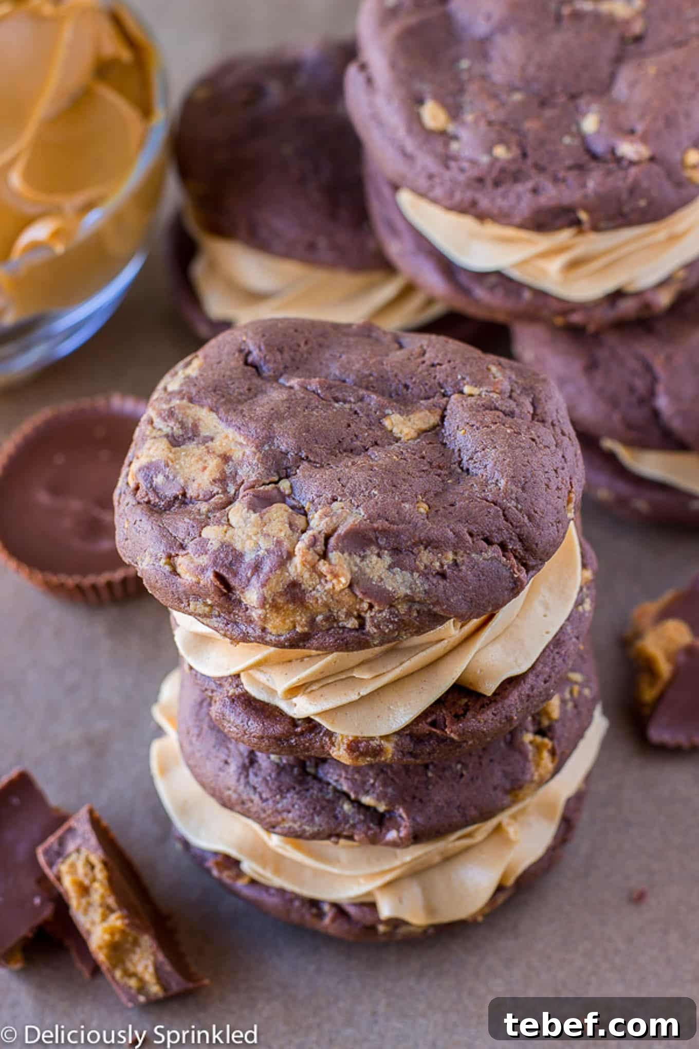 Chocolate peanut butter whoopie pies stacked on the counter with crumbled peanut butter cups.