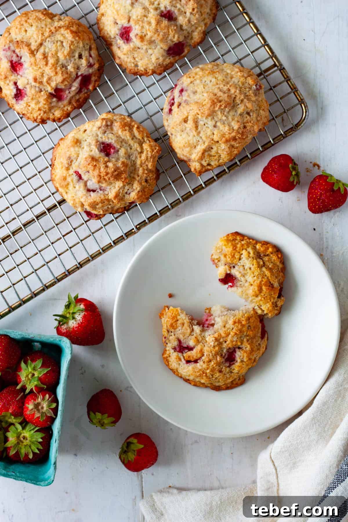 A strawberry biscuit broken in half on a small plate with more strawberry biscuits on a wire rack.