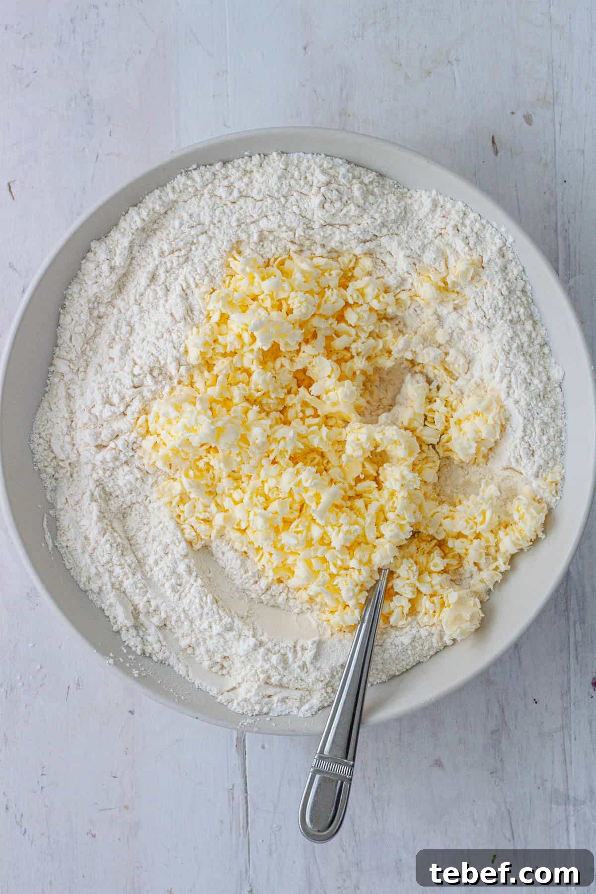 Grated butter in a bowl with the dry ingredients for drop biscuits.