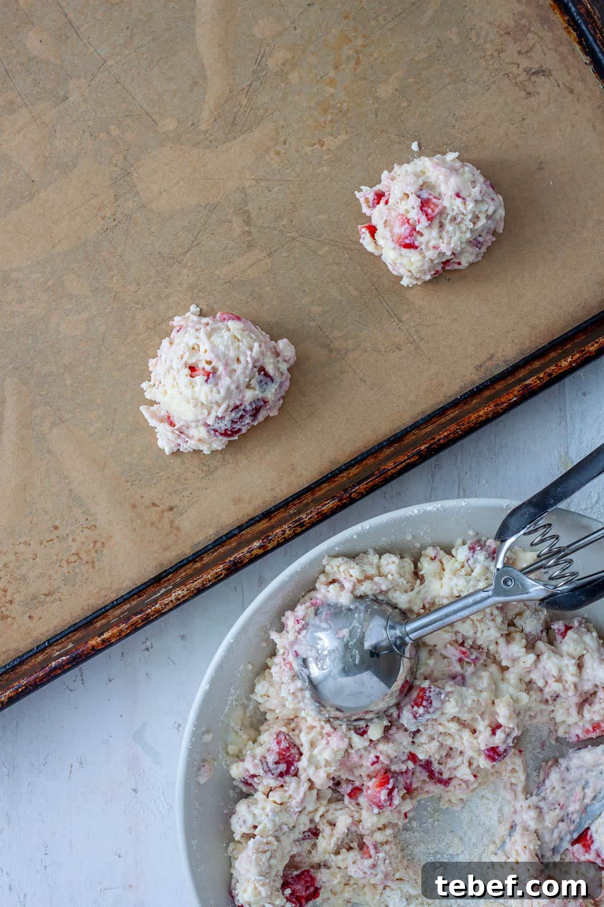Strawberry biscuits getting scooped and placed on a parchment lined baking sheet.