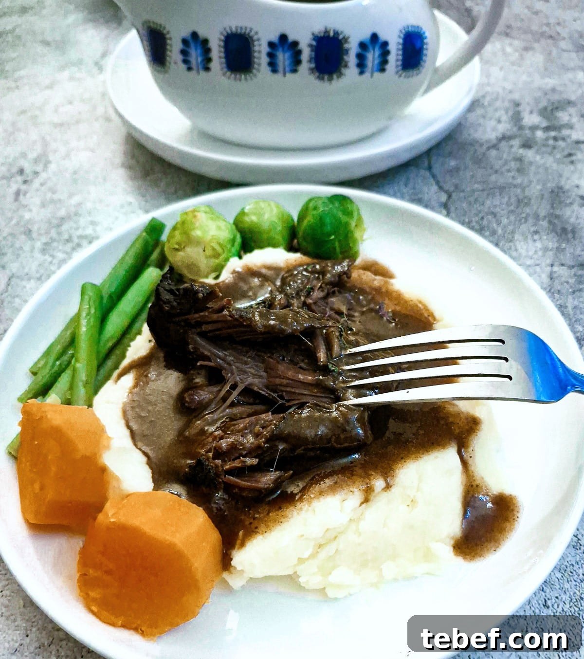 Melt-in-Your-Mouth Slow-Braised Beef Cheeks Recipe 13 Beef cheeks on a pile of mashed potatoes with steamed vegetables amd gravy.