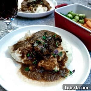 Melt-in-Your-Mouth Slow-Braised Beef Cheeks Recipe 18 A piece of slow-braised beef cheek on a pile of mashed potatoes, with gravy.