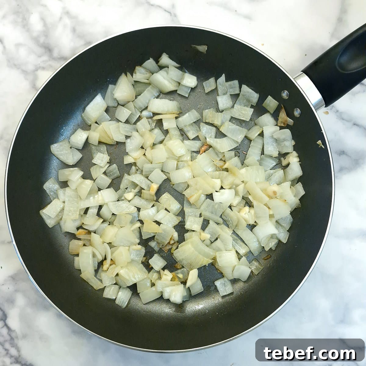 Melt-in-Your-Mouth Slow-Braised Beef Cheeks Recipe 5 Onions softening in a frying pan.