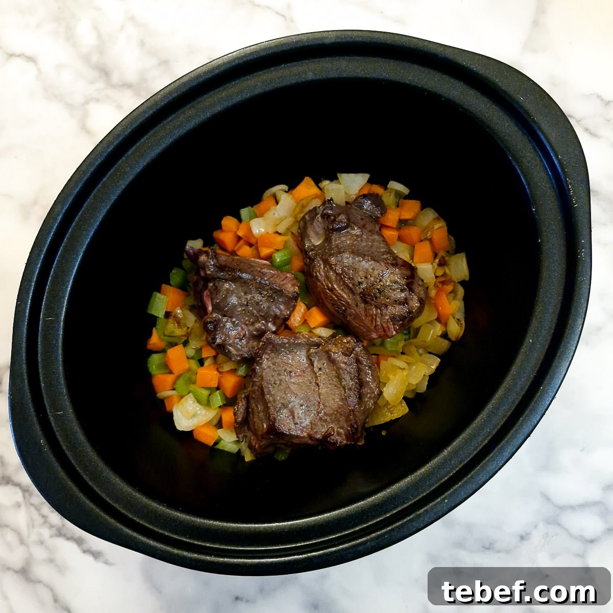 Melt-in-Your-Mouth Slow-Braised Beef Cheeks Recipe 9 Beef cheeks added to vegetables in a slow cooker.