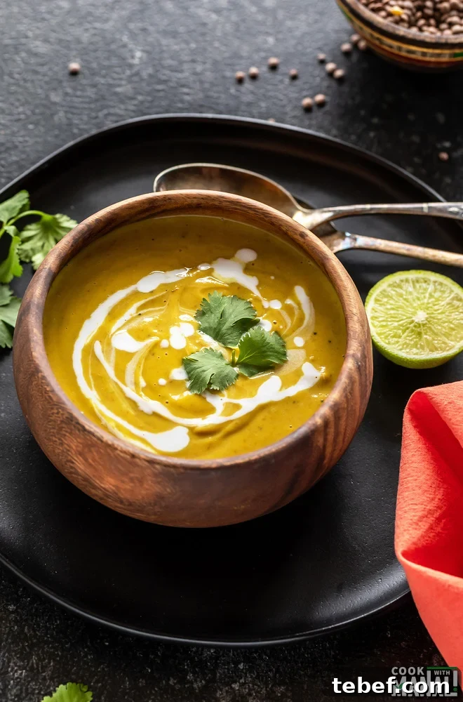 cauliflower lentil soup served in a round wooden bowl and garnished with cilantro with 2 spoons and a cut lime placed on the side