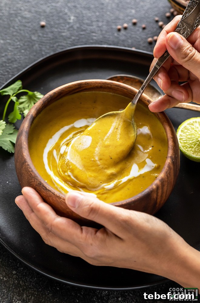 pair of hands holding a wooden bowl full of soup with one hand holding a spoon into the bowl