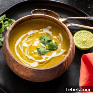 cauliflower lentil soup served in a round wooden bowl and garnished with cilantro with 2 spoons and a cut lime placed on the side