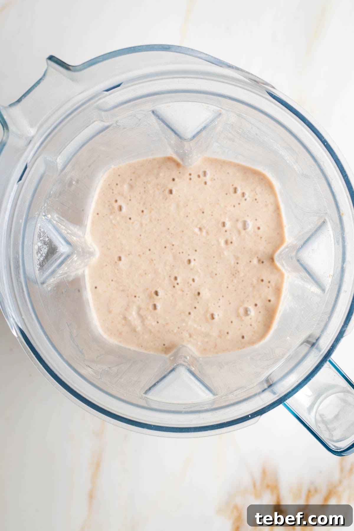 Top view of a blender pitcher with a beige batter with air bubbles.