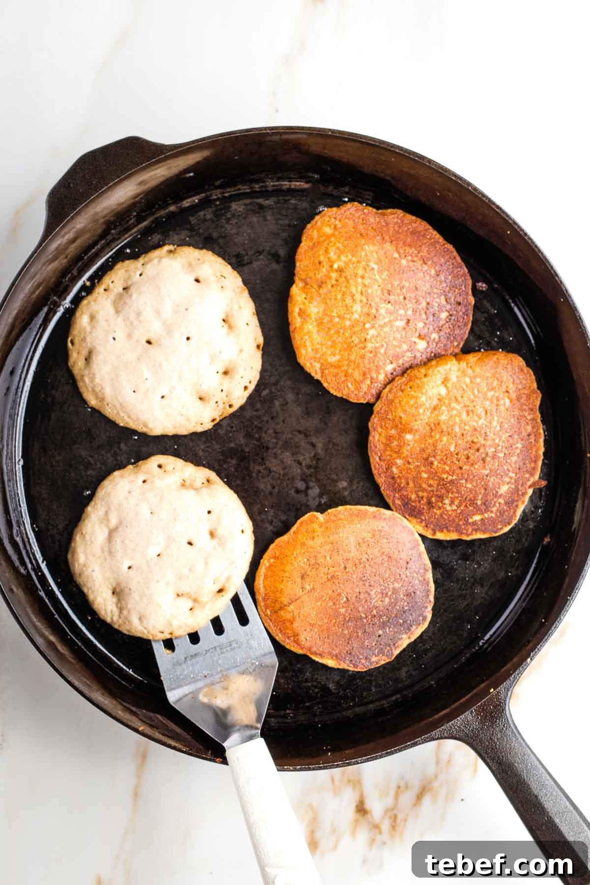 Pancakes with bubbles, and some already flipped in a cast iron skillet.