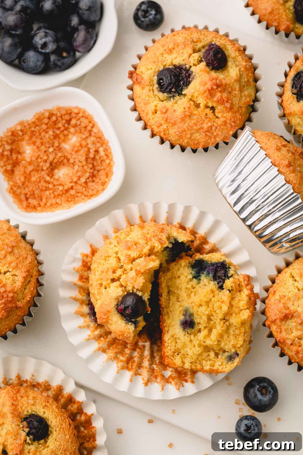 Almond Flour Blueberry Muffins Recipe — Moist Low-Carb Muffins 3 An almond flour blueberry muffin split in half on top of a muffin liner surrounded by other muffins.