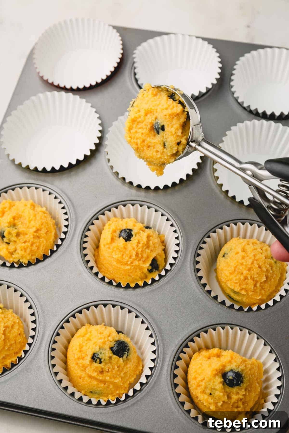 Almond Flour Blueberry Muffins Recipe — Moist Low-Carb Muffins 10 Almond flour blueberry muffin batter being portioned into a muffin tin lined with muffin liners.