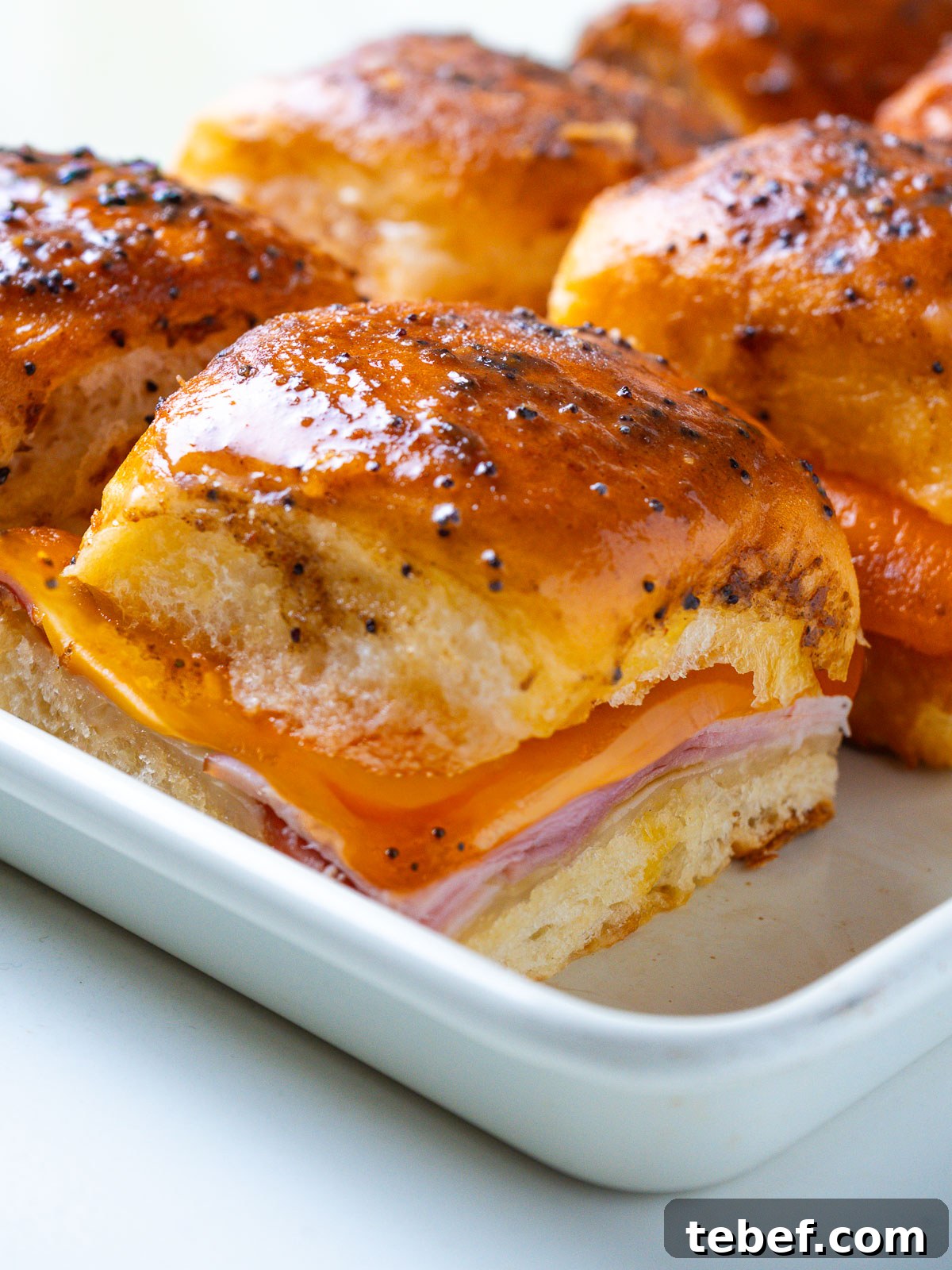 Close-up of a single Hawaiian ham and cheese slider with melted Swiss cheese pulling down the side.