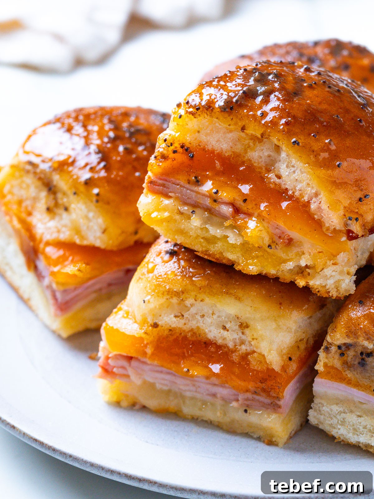 A plate of stacked Hawaiian ham and cheese sliders with a glossy, poppy-seed-flecked glaze.