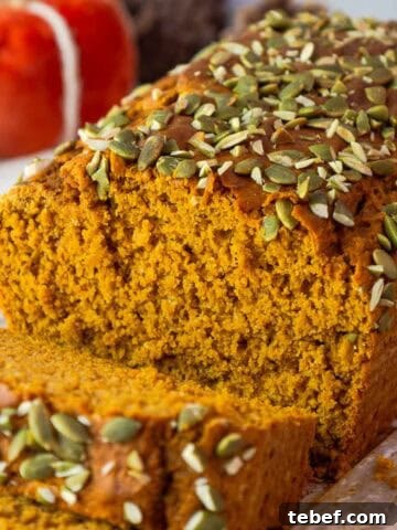 Sliced pumpkin bread showing its fluffy interior and pepita crusted top, set against a fall-themed background.