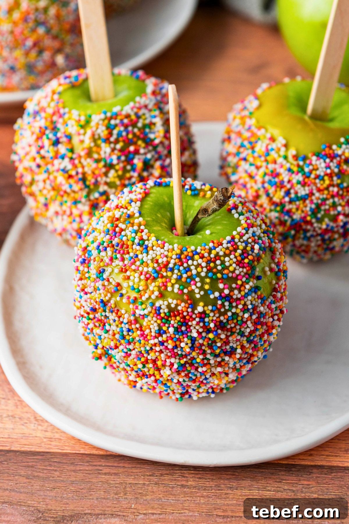 How to Make Classic Caramel Apples at Home in 5 Steps 2 Green apples dipped in a coating and rolled in colorful sprinkles.
