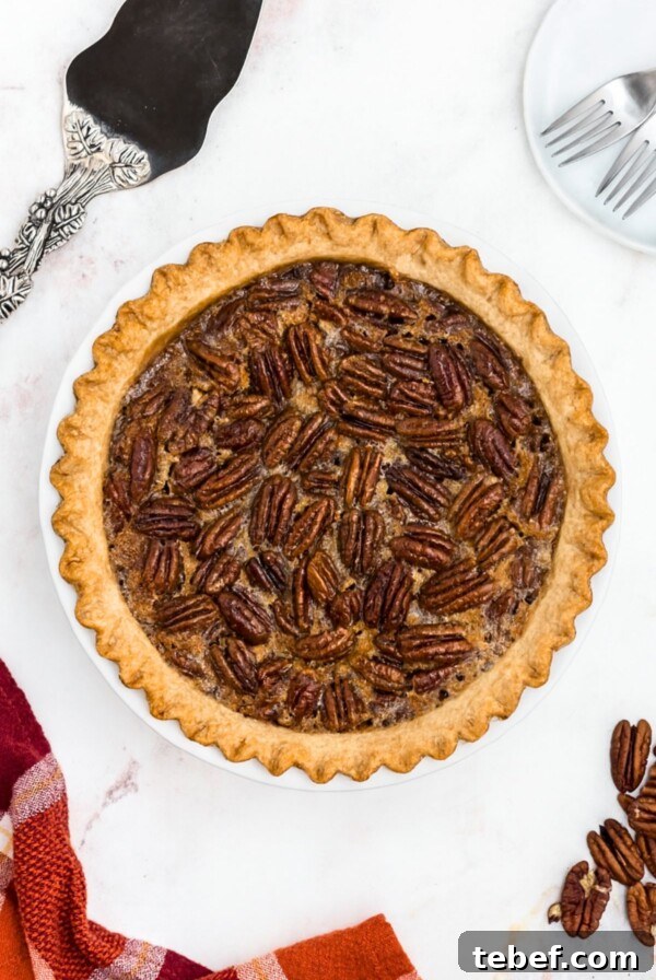 How to Make Classic Caramel Apples at Home in 5 Steps 13 Pecan pie with golden fluted crust on a marble table with spatula and pecans on the table.