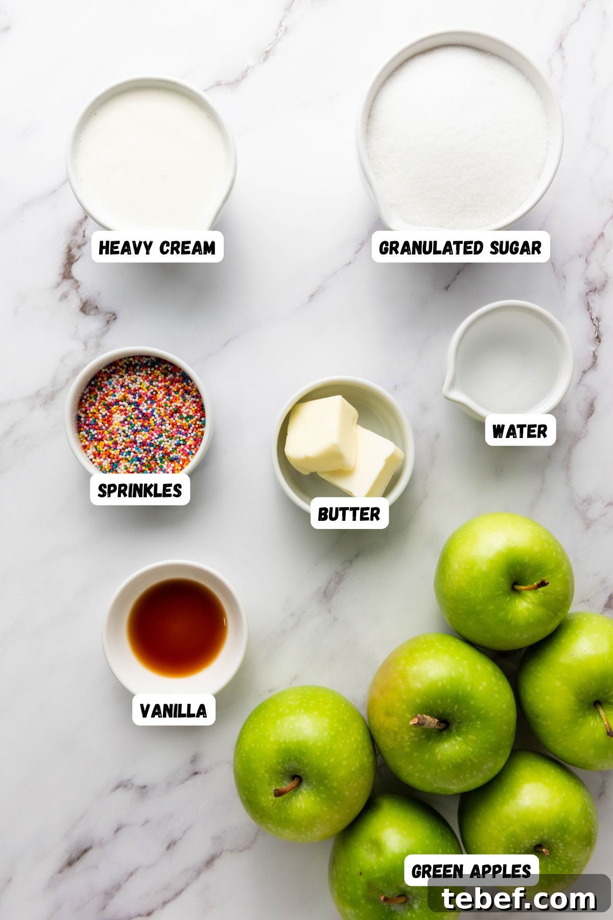 How to Make Classic Caramel Apples at Home in 5 Steps 3 Apples, sugar, butter, and other ingredients, measured into small containers on a black and white marble table.
