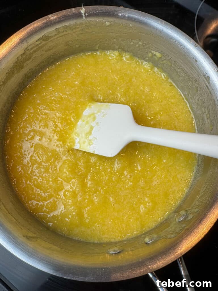 Classic Pineapple Icing Recipe for Cakes and Cupcakes 11 Spatula stirring a drained can of crushed pineapple into a pan of homemade icing.