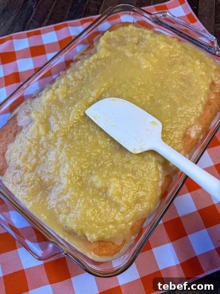 Classic Pineapple Icing Recipe for Cakes and Cupcakes 3 Spatula spreading light, citrusy and enjoyable pineapple icing over top of a cake on an orange and white plaid napkin.