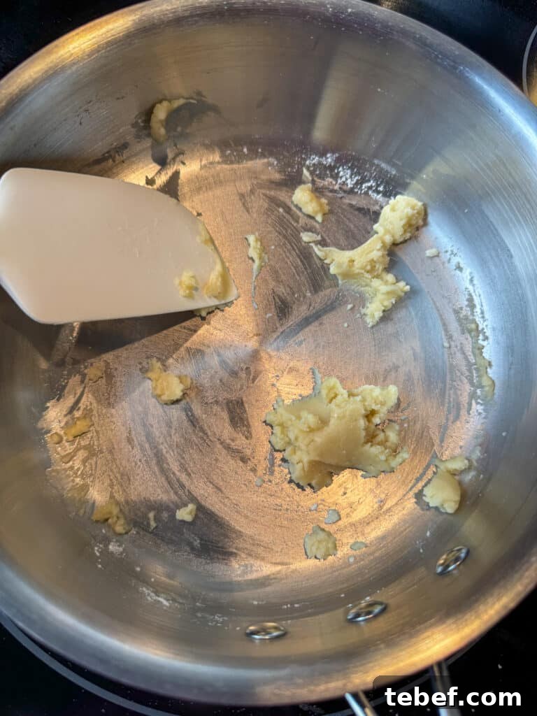Classic Pineapple Icing Recipe for Cakes and Cupcakes 6 Spatula stirring butter and flour together to make a paste over heat in a silver pan.