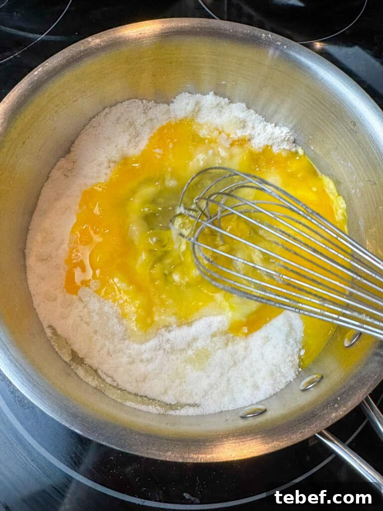 Classic Pineapple Icing Recipe for Cakes and Cupcakes 7 Whisk stirring eggs into sugar, flour and butter mixture in a sauce pan.
