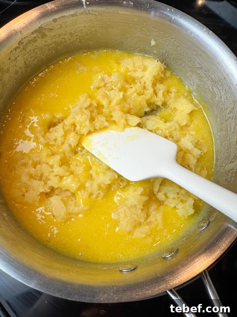 Classic Pineapple Icing Recipe for Cakes and Cupcakes 9 Drained crushed pineapple being stirred into butter, flour and sugar mixture in a silver sauce pan.