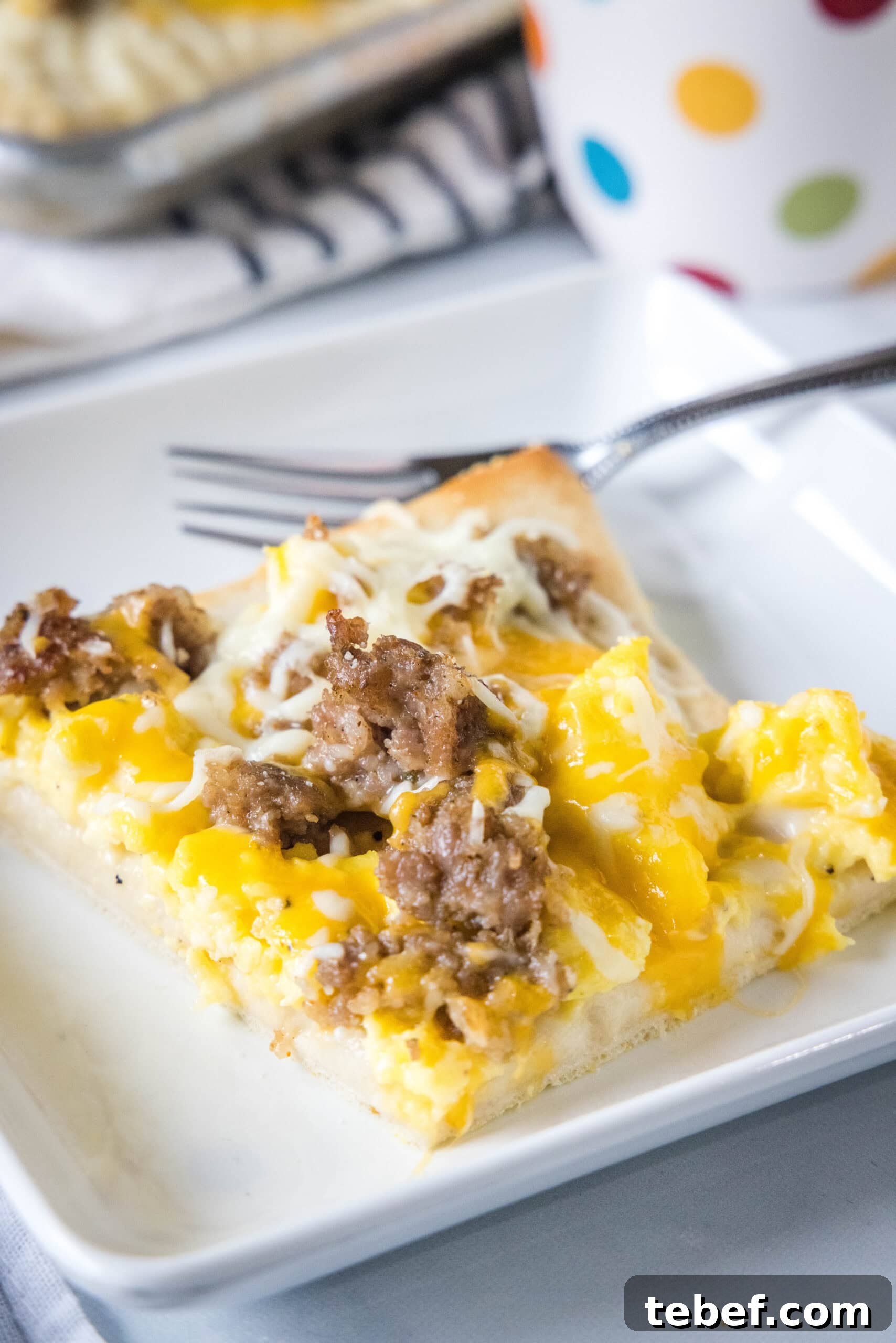 This satisfying breakfast pizza combines all of your breakfast favorites on top of a crispy pizza crust. It's so easy, baked in a sheet pan! A slice of breakfast pizza on a white plate next to a fork.
