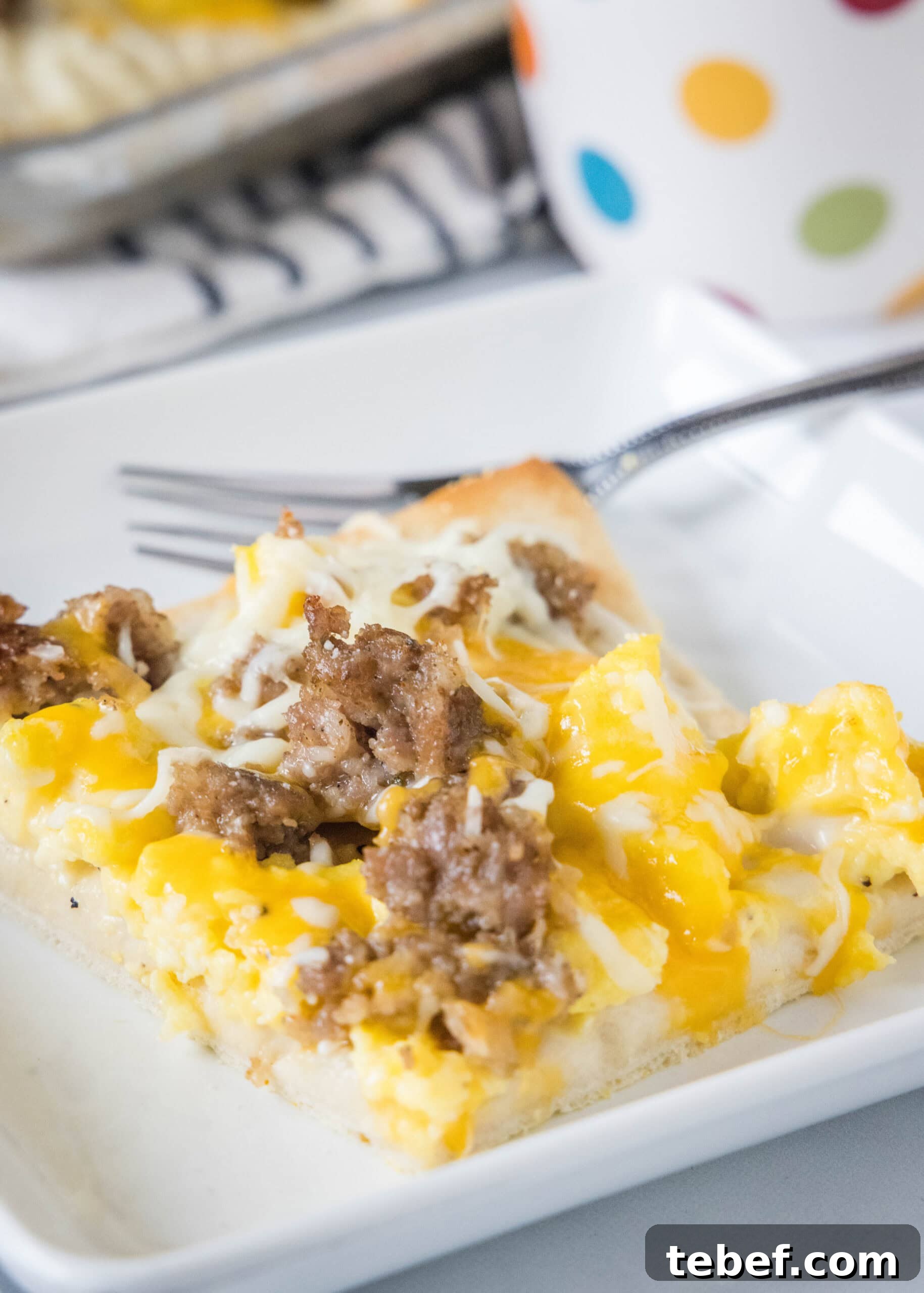 This satisfying breakfast pizza combines all of your breakfast favorites on top of a crispy pizza crust. It's so easy, baked in a sheet pan! A slice of breakfast pizza on a white plate next to a fork.
