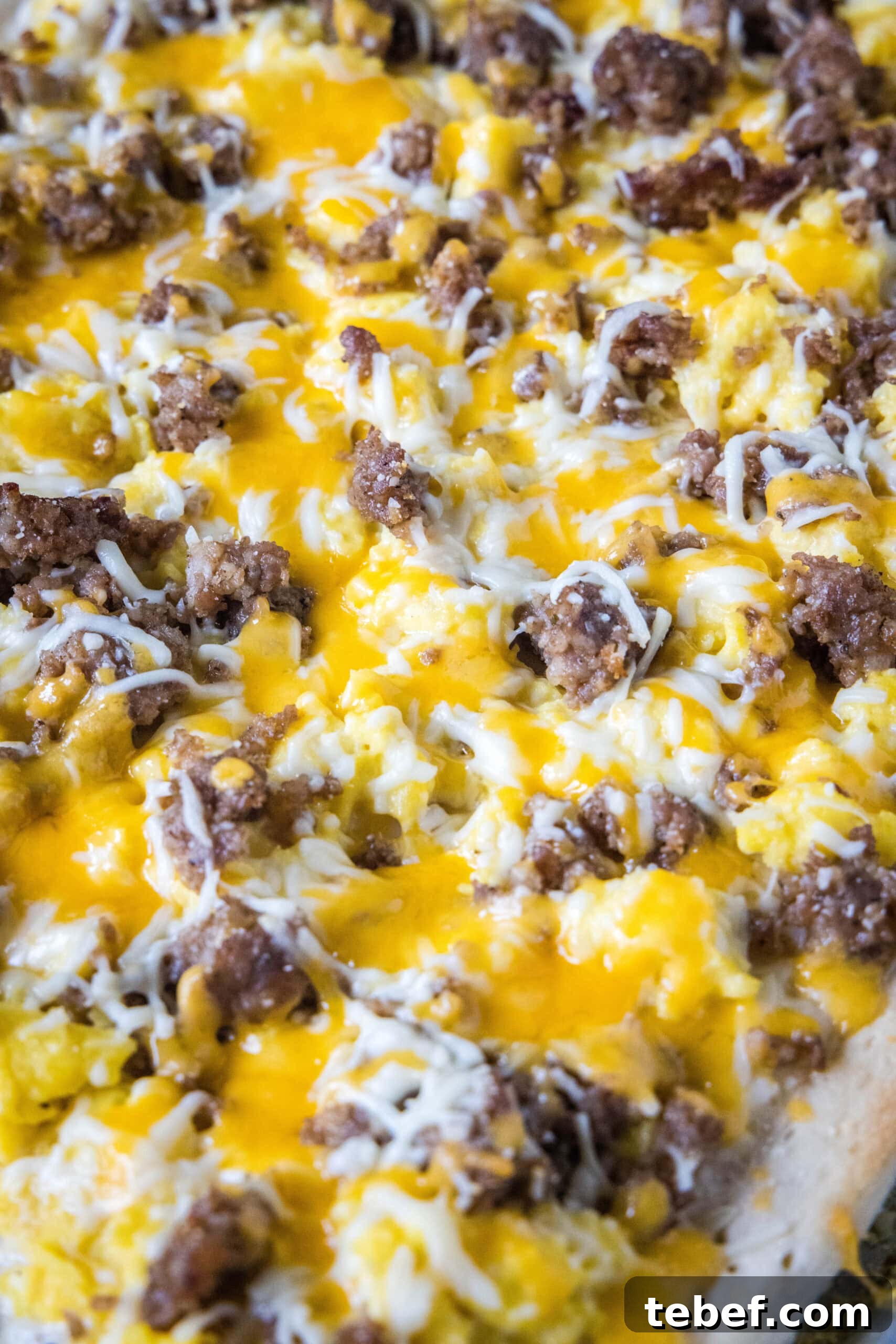 This satisfying breakfast pizza combines all of your breakfast favorites on top of a crispy pizza crust. It's so easy, baked in a sheet pan! Close up of a baked breakfast pizza topped with sausage, egg, and cheese.