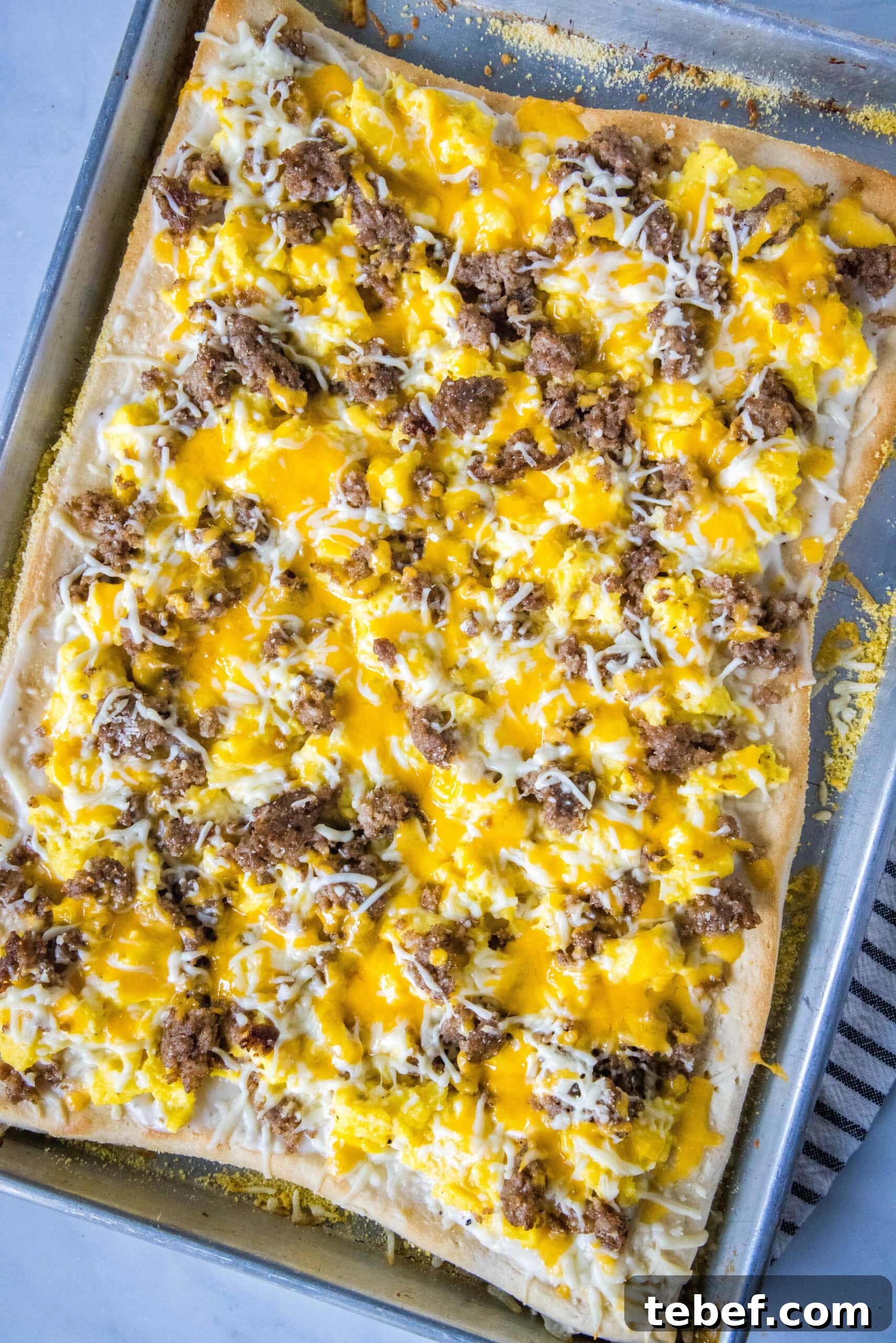 This satisfying breakfast pizza combines all of your breakfast favorites on top of a crispy pizza crust. It's so easy, baked in a sheet pan! Overhead view of a baked breakfast pizza in a sheet pan.