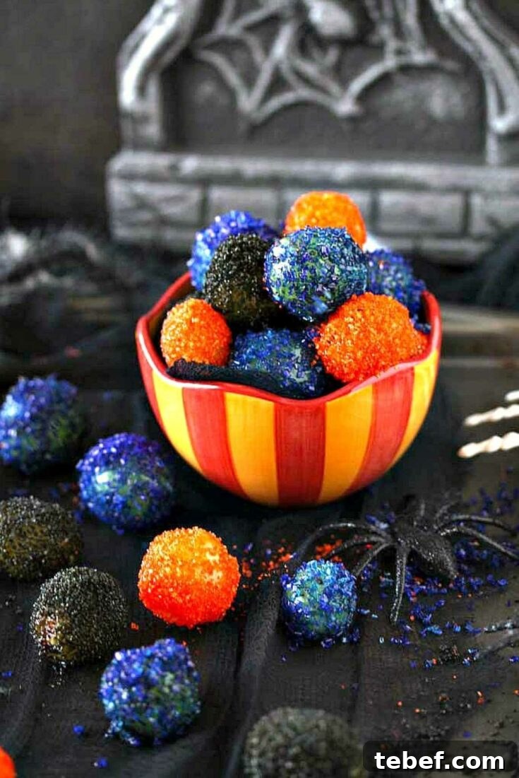 Red and yellow striped bowl filled with colorful grapes, with others nearby amongst Halloween decorations.