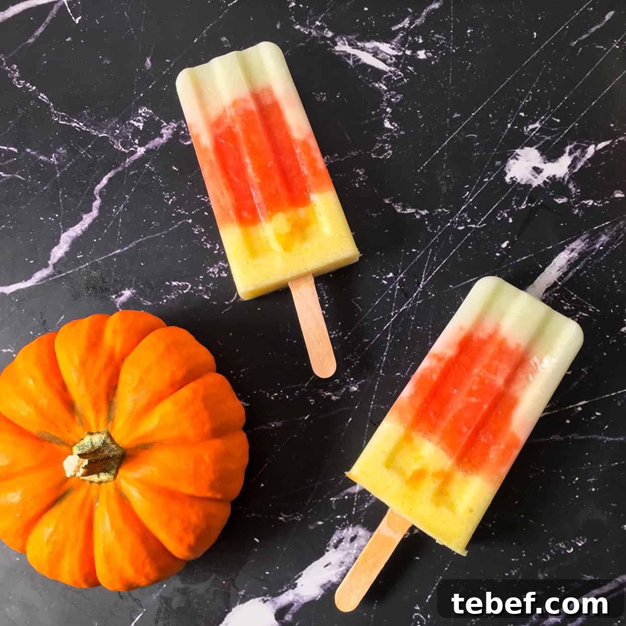 Two fruit pops laying on black surface with decorative mini pumpkin.