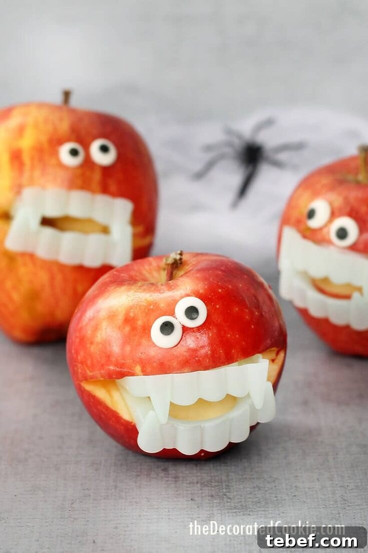 Three apples turned into Halloween monsters with googly eyes and vampire teether, with decorative gauze and spider in background.