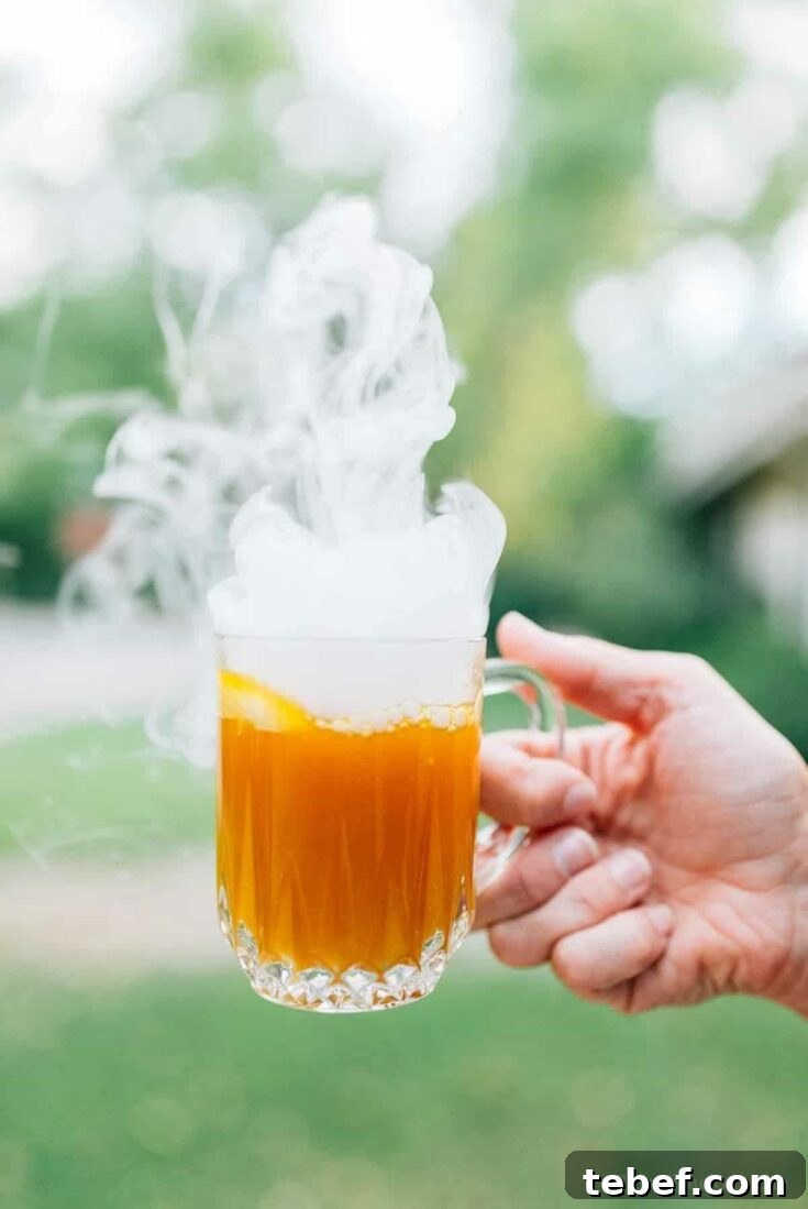 Hand holding crystal mug of punch with dry ice steam rising out of it.