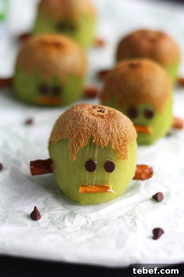 Several fruit Frankensteins arranged on crinkly white paper with mini chocolate chips scattered about.